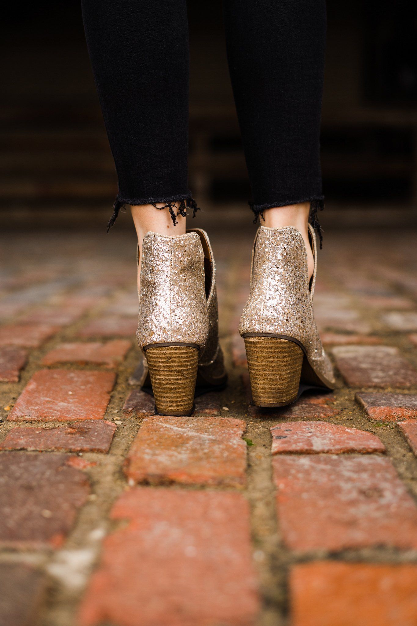 Back view of woman wearing Fiera gold glitter booties showing glitter detail.