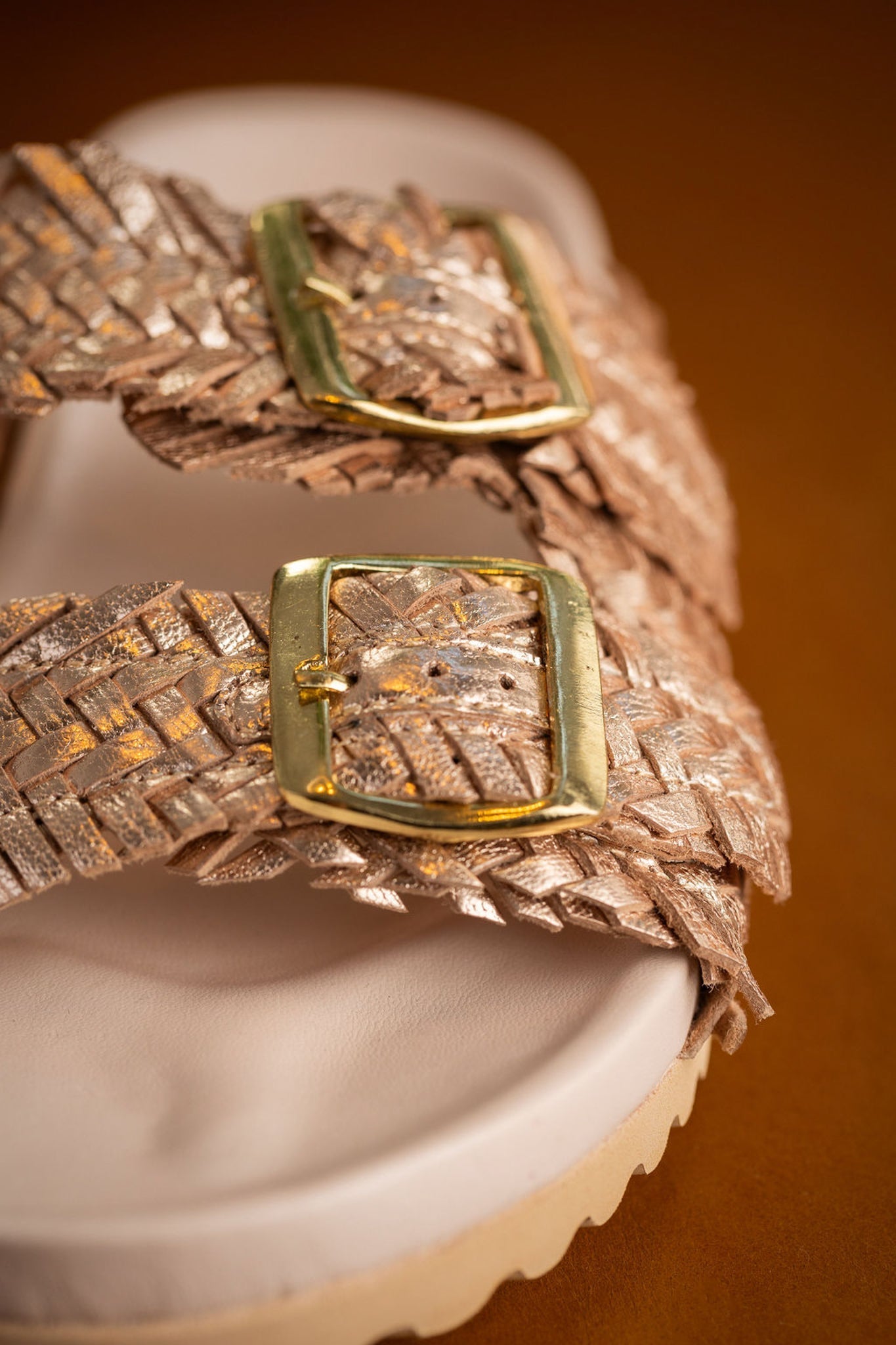 Close up of champagne woven leather straps and cushioned footbed with adjustable buckles.