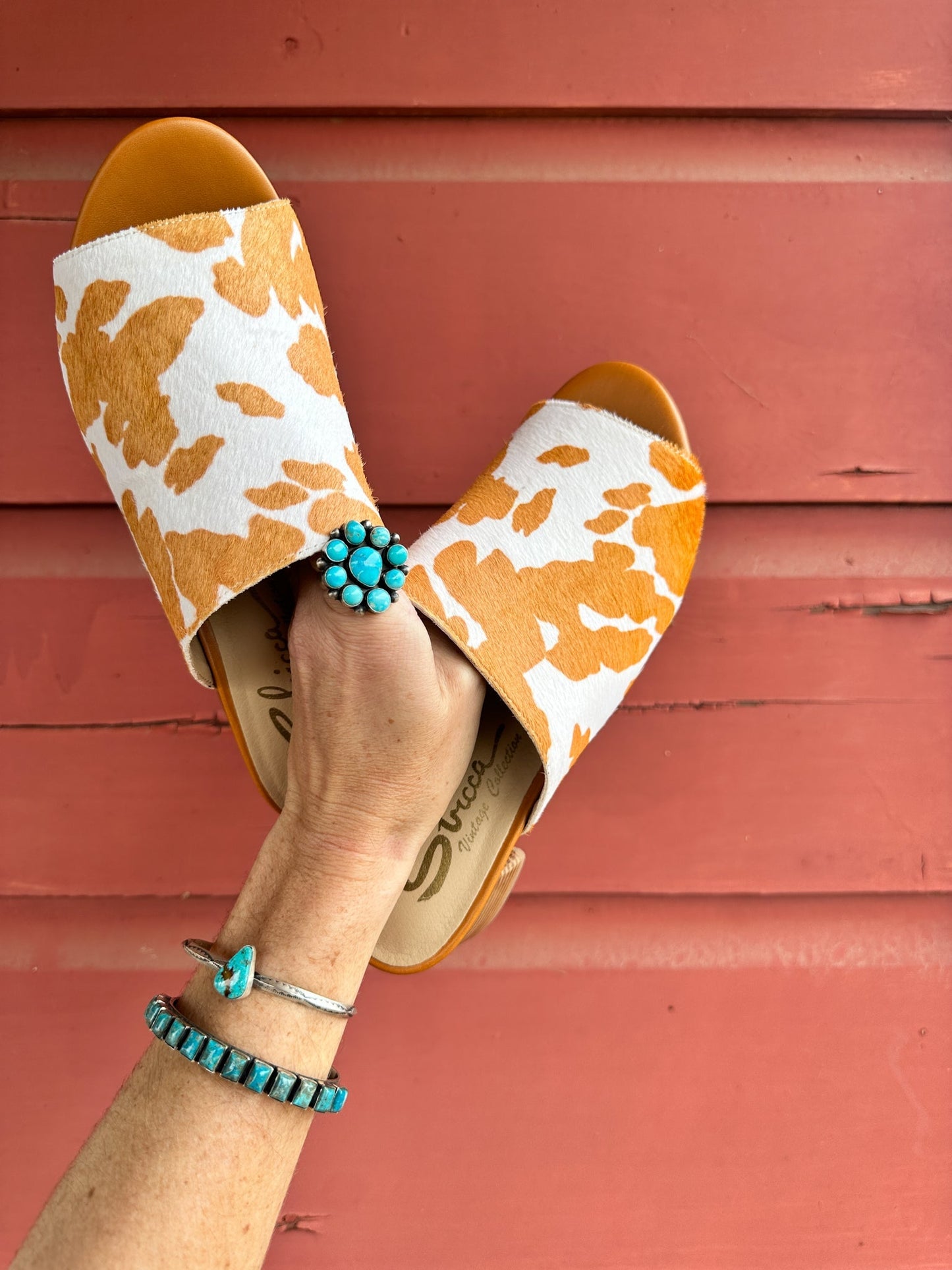 Top front view of woman holding Prairie Tan Cowhide Slides with bold tan-and-white calf-hair cow print design