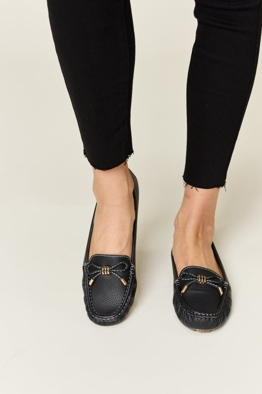 Black Wrenly Bow Flats with white stitching and slip-on design.