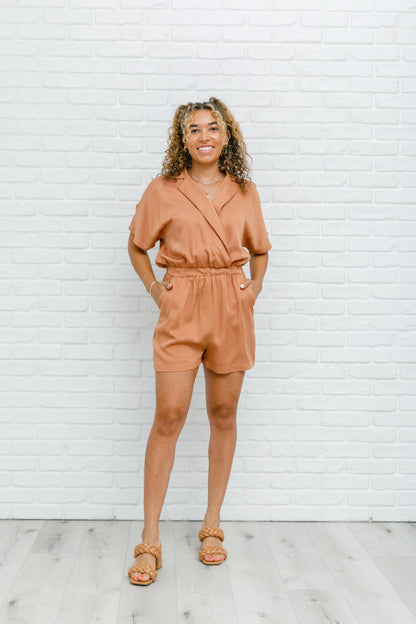 Camel-colored romper with a collared V-neckline, short sleeves, an elastic waistband, and functional pockets.