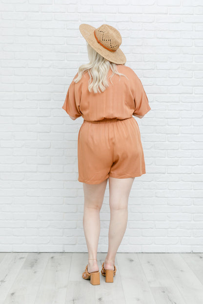 Camel-colored romper with a collared V-neckline, short sleeves, an elastic waistband, and functional pockets.