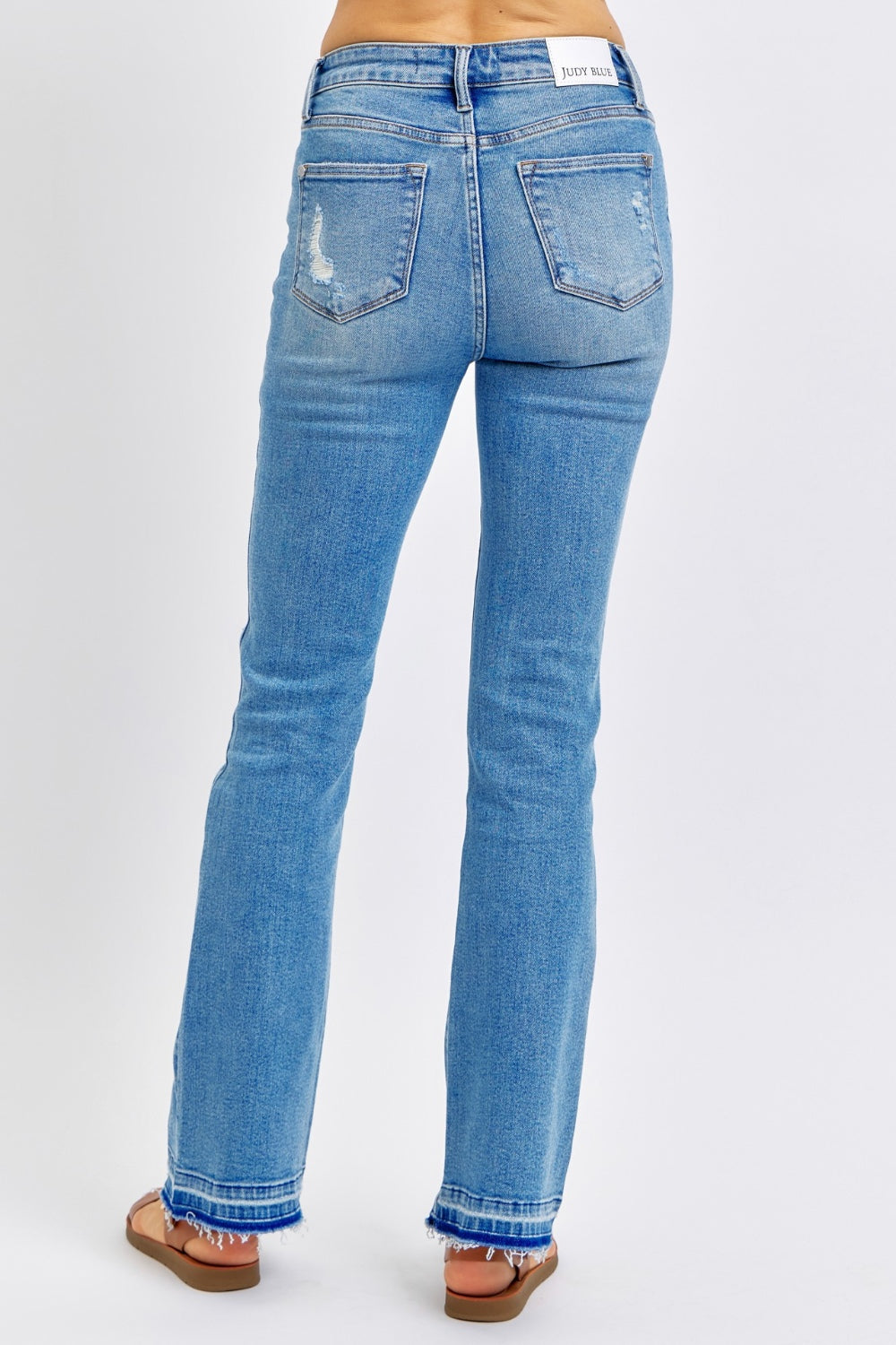 Medium wash mid-rise jeans with distressed detailing and destroyed hem, featuring a comfortable fit and moderate stretch.