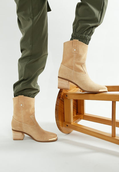 Beige Emberly boots on model with stacked heel and curved Western cut.