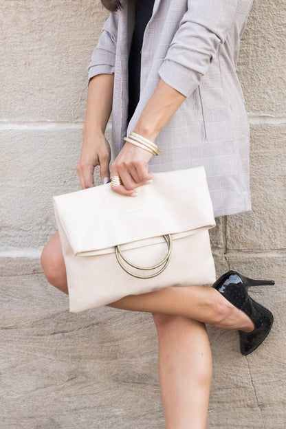 Woman carrying bone Safara Fold-Over Clutch with antique bronze O-ring accents.