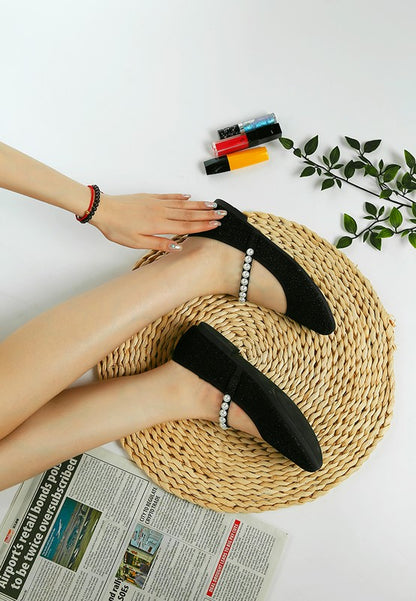 Top side view of woman wearing both black Corphee Pearl Strapped Glitter Ballerinas with round toe and pearl strap detail.