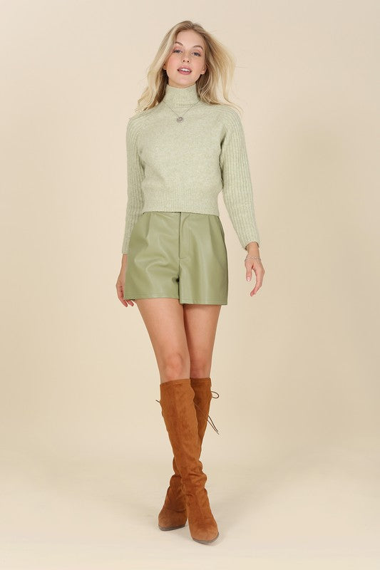 Trendy green vegan leather shorts featuring a hook and zipper closure, side pockets, pin-tuck detailing, and a comfortable wide elastic waistband.