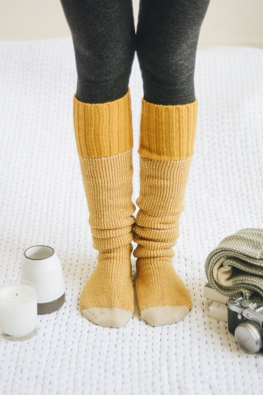 Woman standing wearing mustard Jerica Lounge Socks, knee-high with cozy knit detail.