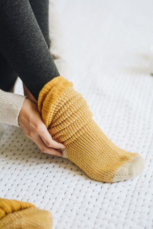 Woman sitting in mustard Jerica Knitted Lounge Socks with soft oversized knit texture.