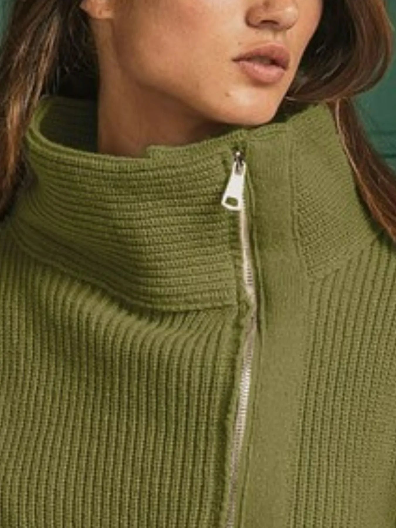 Close-up of Maura sweater jacket showing ribbed knit fabric, high neckline, and zipper detail in olive green.