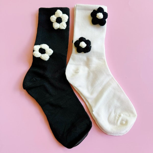 Flat lay close-up showing daisy embellishments on both black and white socks.