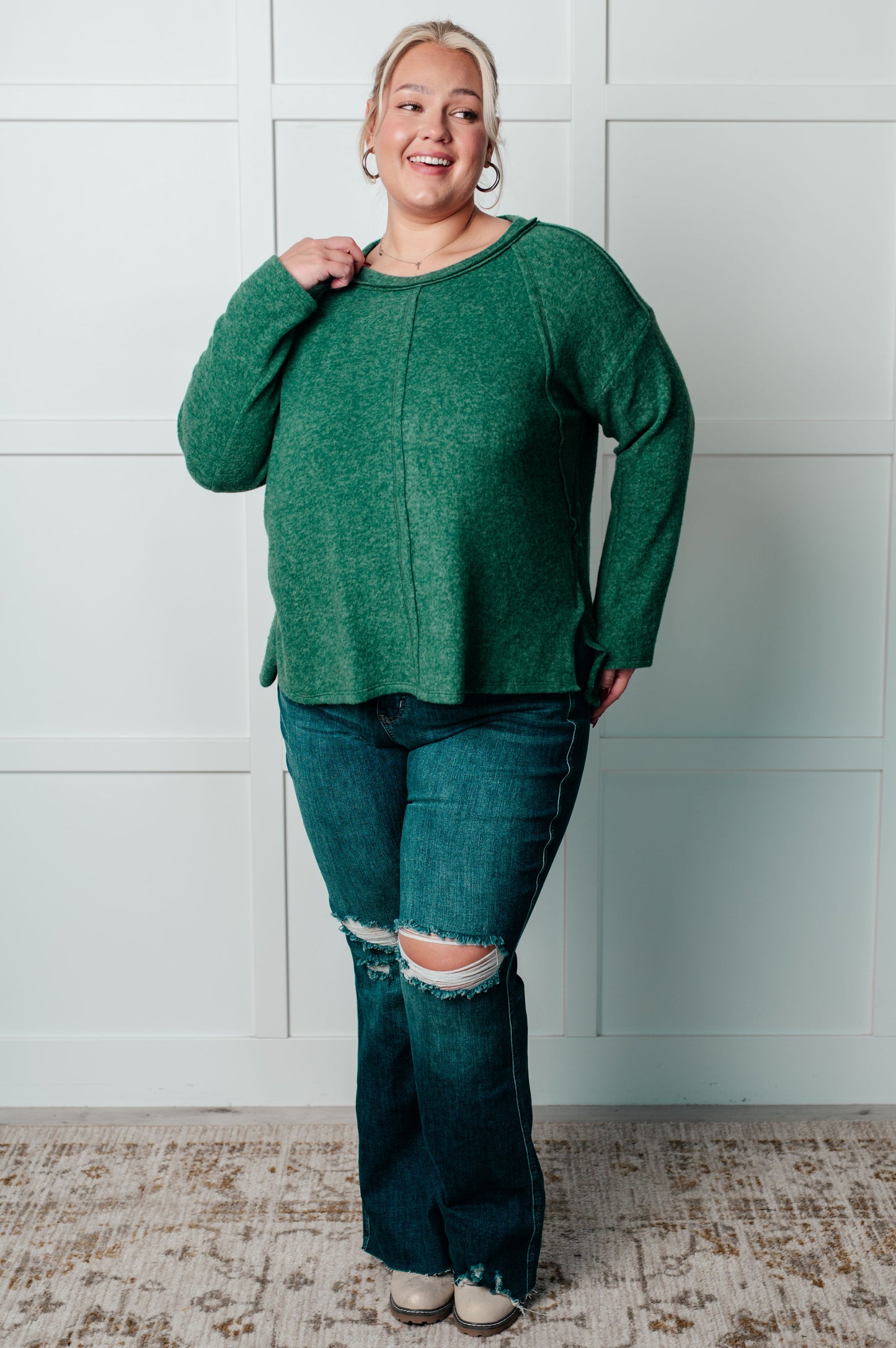 Women's Brushed Hacci Sweater in dark green featuring a round neckline, drop shoulders, stepped hemline, side slits, and raw seams. 