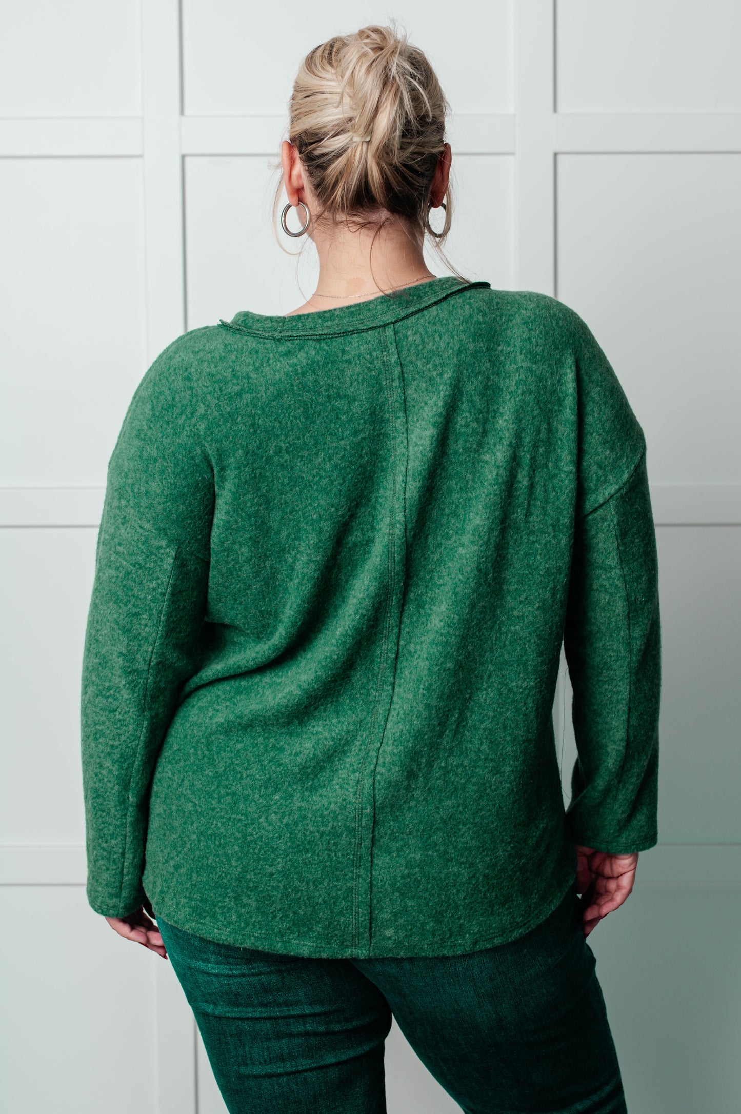 Women's Brushed Hacci Sweater in dark green featuring a round neckline, drop shoulders, stepped hemline, side slits, and raw seams. 