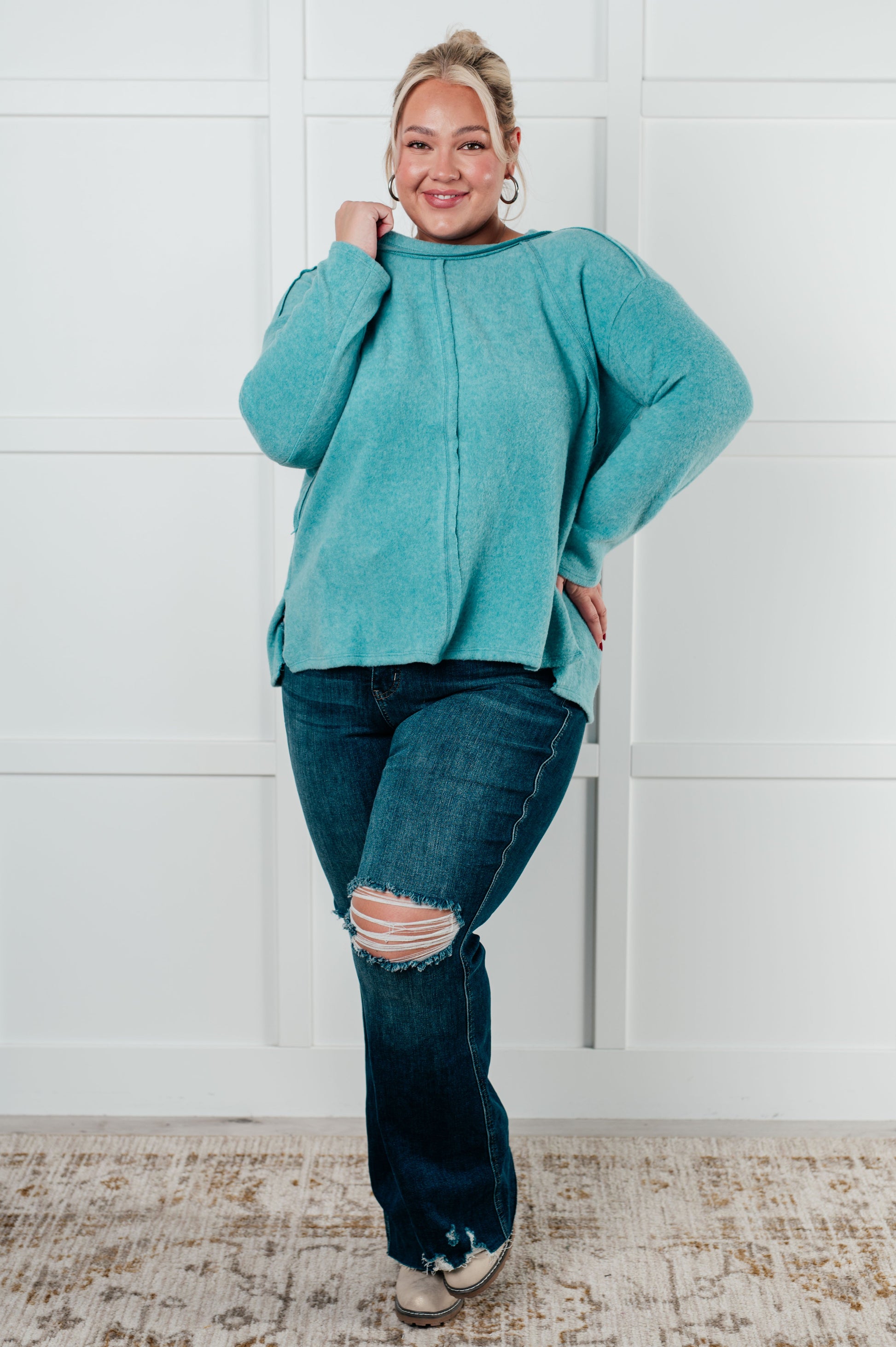 Women's Brushed Hacci Sweater in dusty teal featuring a round neckline, drop shoulders, stepped hemline, side slits, and raw seams. 