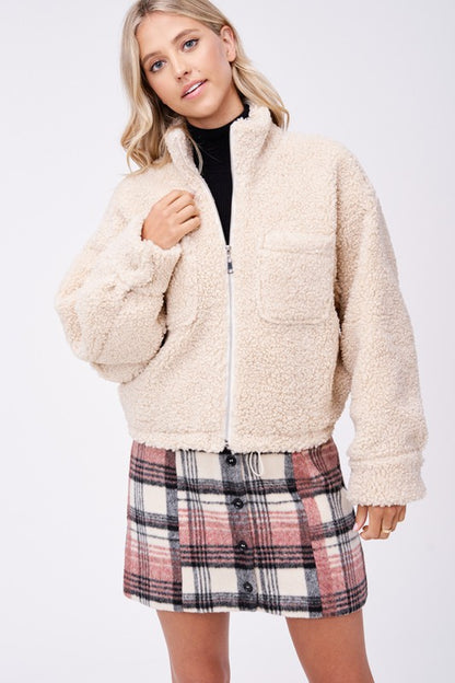 Front view of cream sherpa jacket partially zipped with plaid skirt