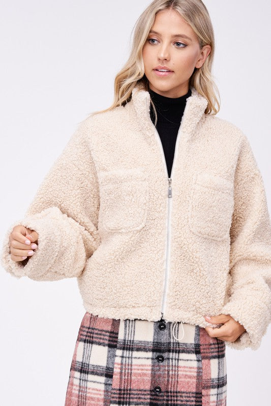 Front view of cream sherpa jacket fully zipped showing chest pockets