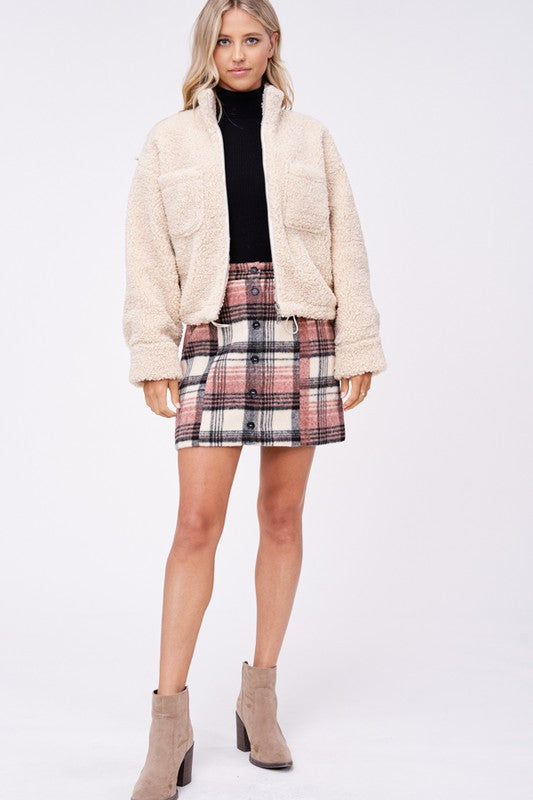 Full body view of cream sherpa jacket styled with plaid skirt and boots
