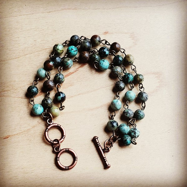 A handcrafted triple-strand bracelet featuring vibrant African turquoise beads, each uniquely patterned. Measures 7.5" in length, offering an earthy and elegant touch. Ideal for layering or wearing alone.