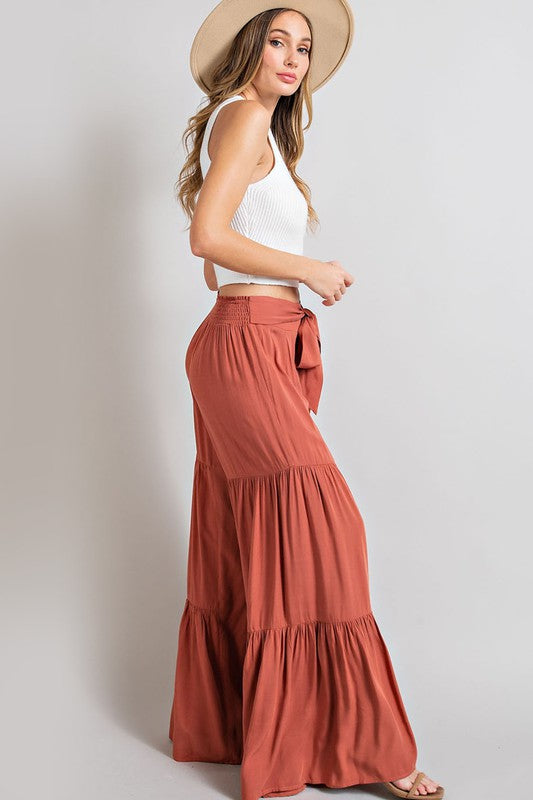 Terracotta wide-leg, tiered pants with a smocked waist and tie front, offering a comfortable, oversized fit for a relaxed, casual look.