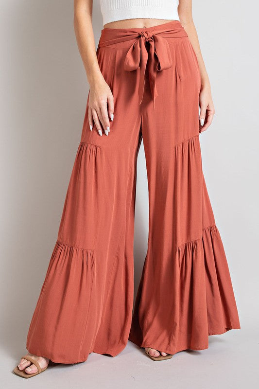 Terracotta wide-leg, tiered pants with a smocked waist and tie front, offering a comfortable, oversized fit for a relaxed, casual look.