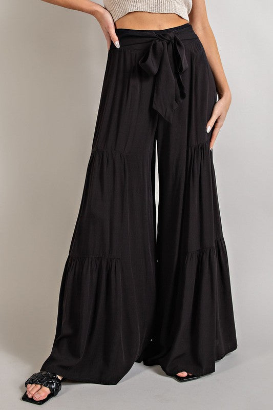 Black wide-leg, tiered pants with a smocked waist and tie front, offering a comfortable, oversized fit for a relaxed, casual look.