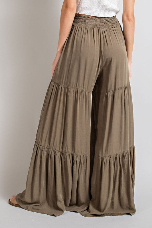 Olive wide-leg, tiered pants with a smocked waist and tie front, offering a comfortable, oversized fit for a relaxed, casual look.