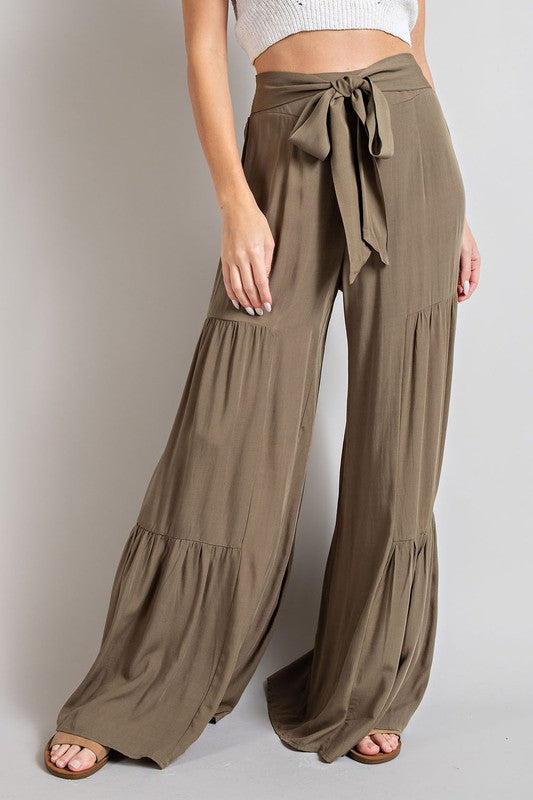 Olive wide-leg, tiered pants with a smocked waist and tie front, offering a comfortable, oversized fit for a relaxed, casual look.