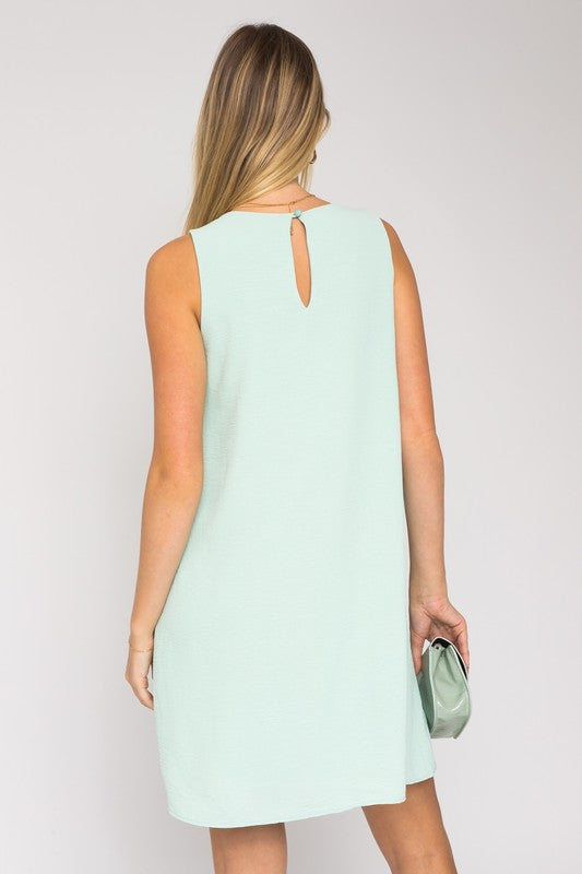 Sleeveless wwing dress in dusty mint features a V-neckline, sleeveless design, and back button closure.