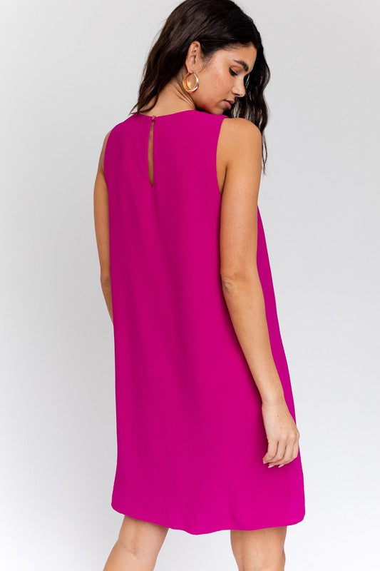 Sleeveless wwing dress in fuchsia features a V-neckline, sleeveless design, and back button closure.