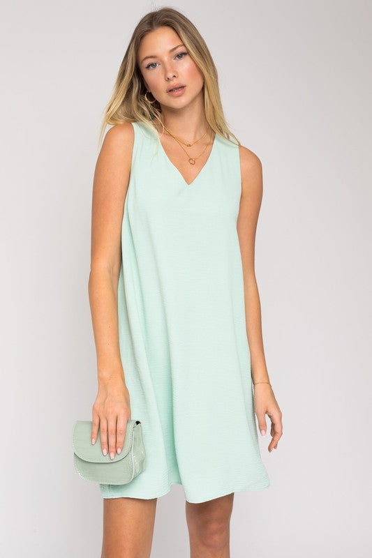 Sleeveless wwing dress in dusty mint features a V-neckline, sleeveless design, and back button closure.