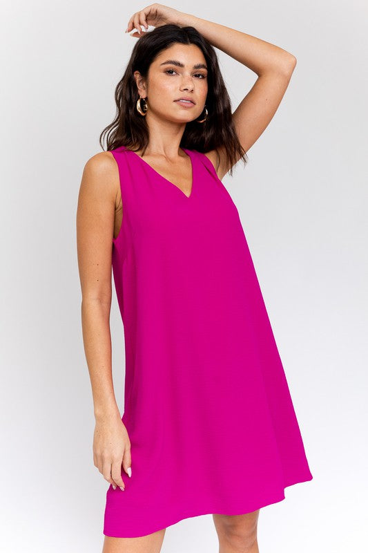 Sleeveless wwing dress in fuchsia features a V-neckline, sleeveless design, and back button closure.