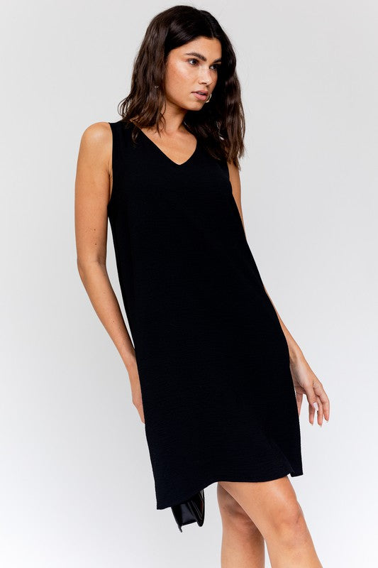 Sleeveless wwing dress in black features a V-neckline, sleeveless design, and back button closure.