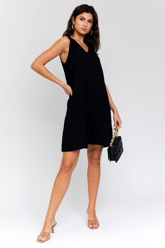 Sleeveless wwing dress in black features a V-neckline, sleeveless design, and back button closure.