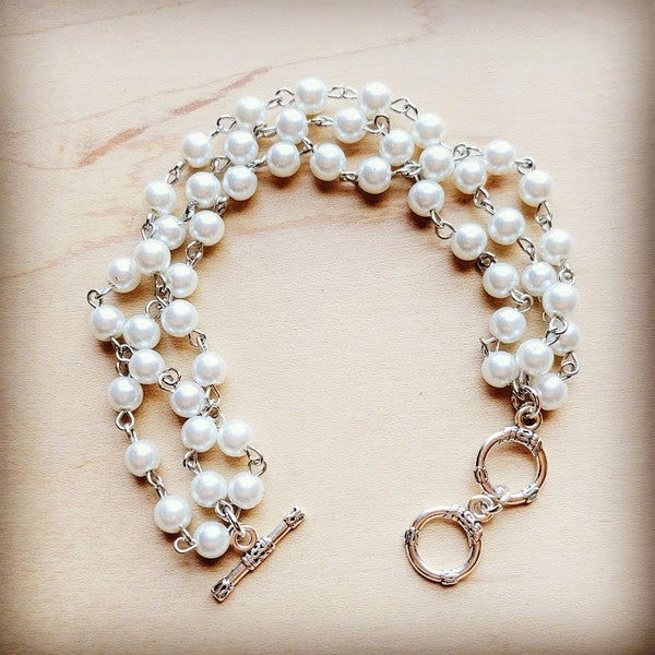 Triple-strand bracelet featuring glass pearls on silver-tone strands, designed with an adjustable length of 7.5 inches.