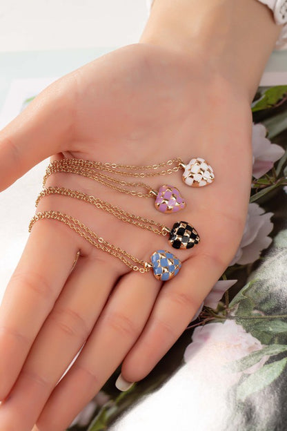 Woman’s hand holding four Mayley Checker Heart Pendant Necklaces in blue, black, pink, and white.