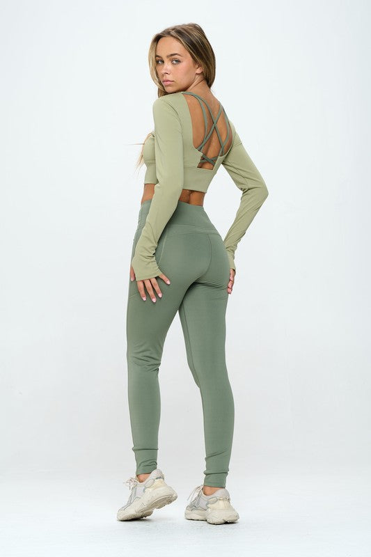 Green two-piece activewear set featuring a cropped top with strap details, long sleeves, and a round neckline, paired with high-waisted, long bottoms.