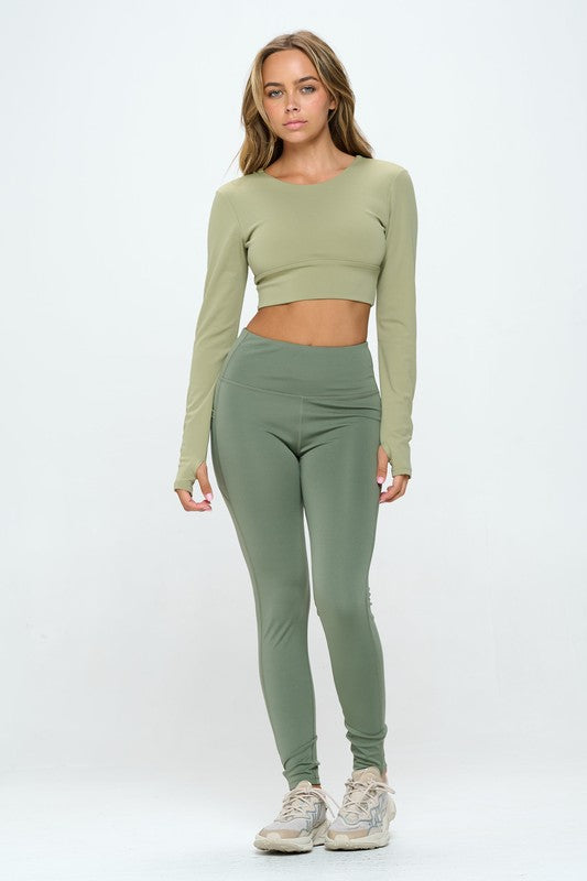 Green two-piece activewear set featuring a cropped top with strap details, long sleeves, and a round neckline, paired with high-waisted, long bottoms.