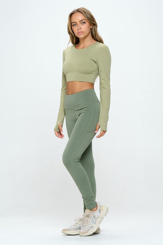 Green two-piece activewear set featuring a cropped top with strap details, long sleeves, and a round neckline, paired with high-waisted, long bottoms.