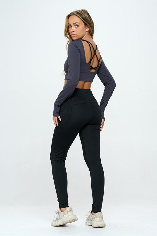 Black two-piece activewear set featuring a cropped top with strap details, long sleeves, and a round neckline, paired with high-waisted, long bottoms.