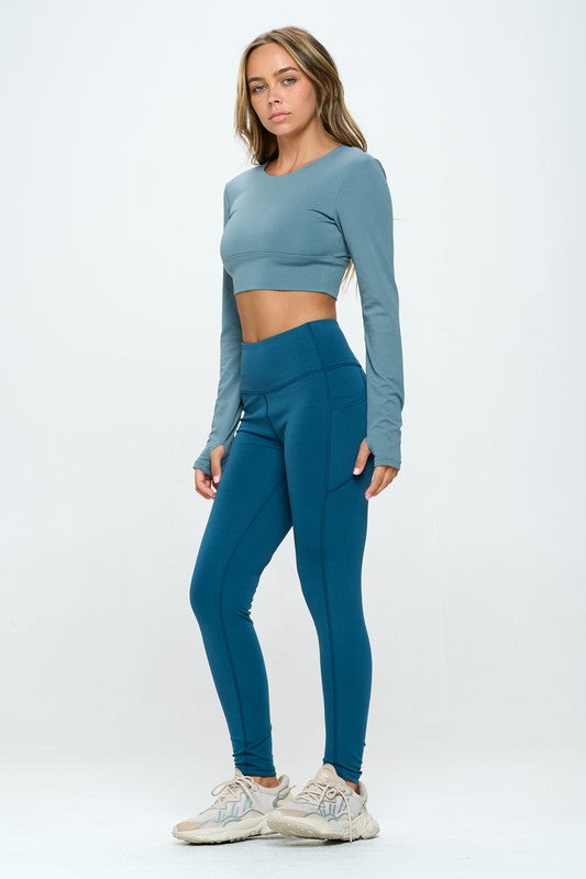 Blue two-piece activewear set featuring a cropped top with strap details, long sleeves, and a round neckline, paired with high-waisted, long bottoms.