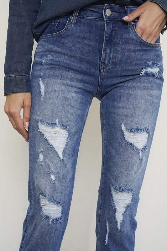 Medium wash distressed girlfriend jeans with a slim fit, mid-rise waist, button closure, and ankle-length cut.