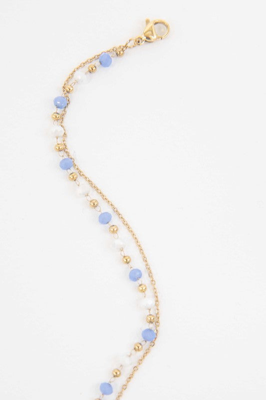 Double-layered Cana beaded bracelet with vibrant blue and white beads and a delicate gold-plated chain.