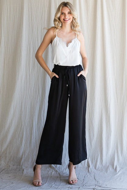 Model wearing Cita Wide Leg Bottoms in Black with high-waisted fit and flowy wide-leg silhouette.