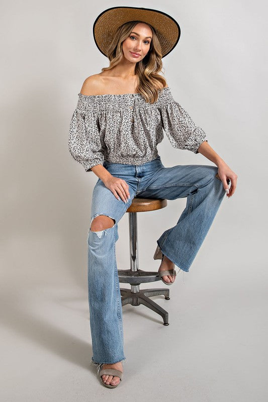 Off white animal print top with smocked off-the-shoulder neckline and button trim. Features a fitted and flared silhouette, 3/4 length puff sleeves, and a romantic, flirty style.