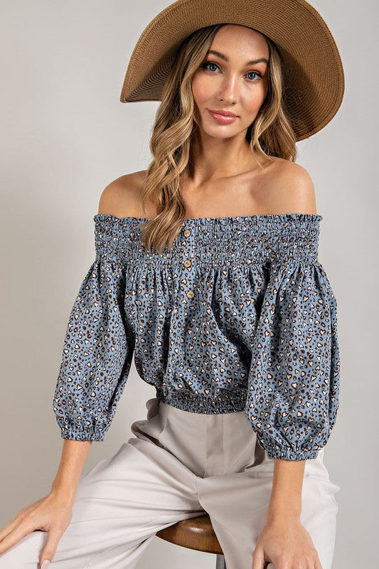 Blue animal print top with smocked off-the-shoulder neckline and button trim. Features a fitted and flared silhouette, 3/4 length puff sleeves, and a romantic, flirty style.