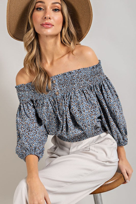 Blue animal print top with smocked off-the-shoulder neckline and button trim. Features a fitted and flared silhouette, 3/4 length puff sleeves, and a romantic, flirty style.