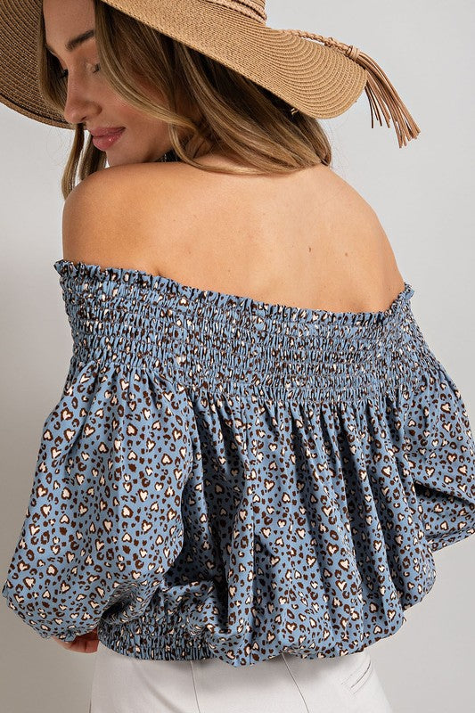 Blue animal print top with smocked off-the-shoulder neckline and button trim. Features a fitted and flared silhouette, 3/4 length puff sleeves, and a romantic, flirty style.