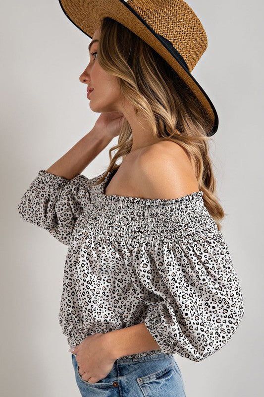 Off white animal print top with smocked off-the-shoulder neckline and button trim. Features a fitted and flared silhouette, 3/4 length puff sleeves, and a romantic, flirty style.