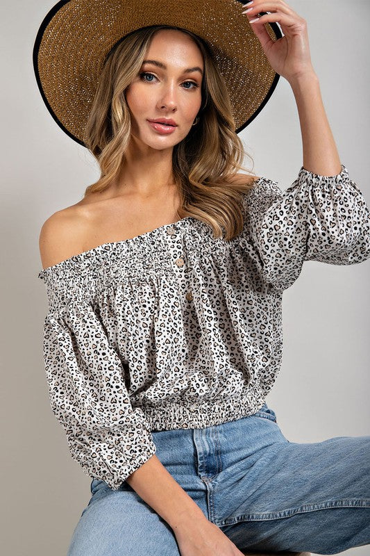 Off white animal print top with smocked off-the-shoulder neckline and button trim. Features a fitted and flared silhouette, 3/4 length puff sleeves, and a romantic, flirty style.