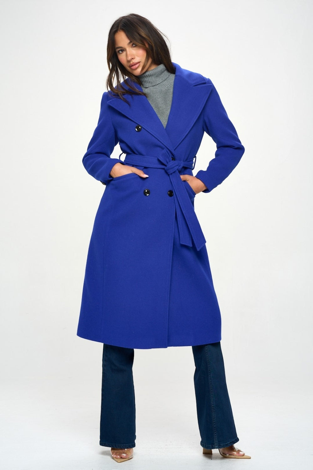 A royal blue double-breasted longline coat with a waist-cinching belt and long sleeves. The coat features a collared neckline, pocket details, and a tied closure.